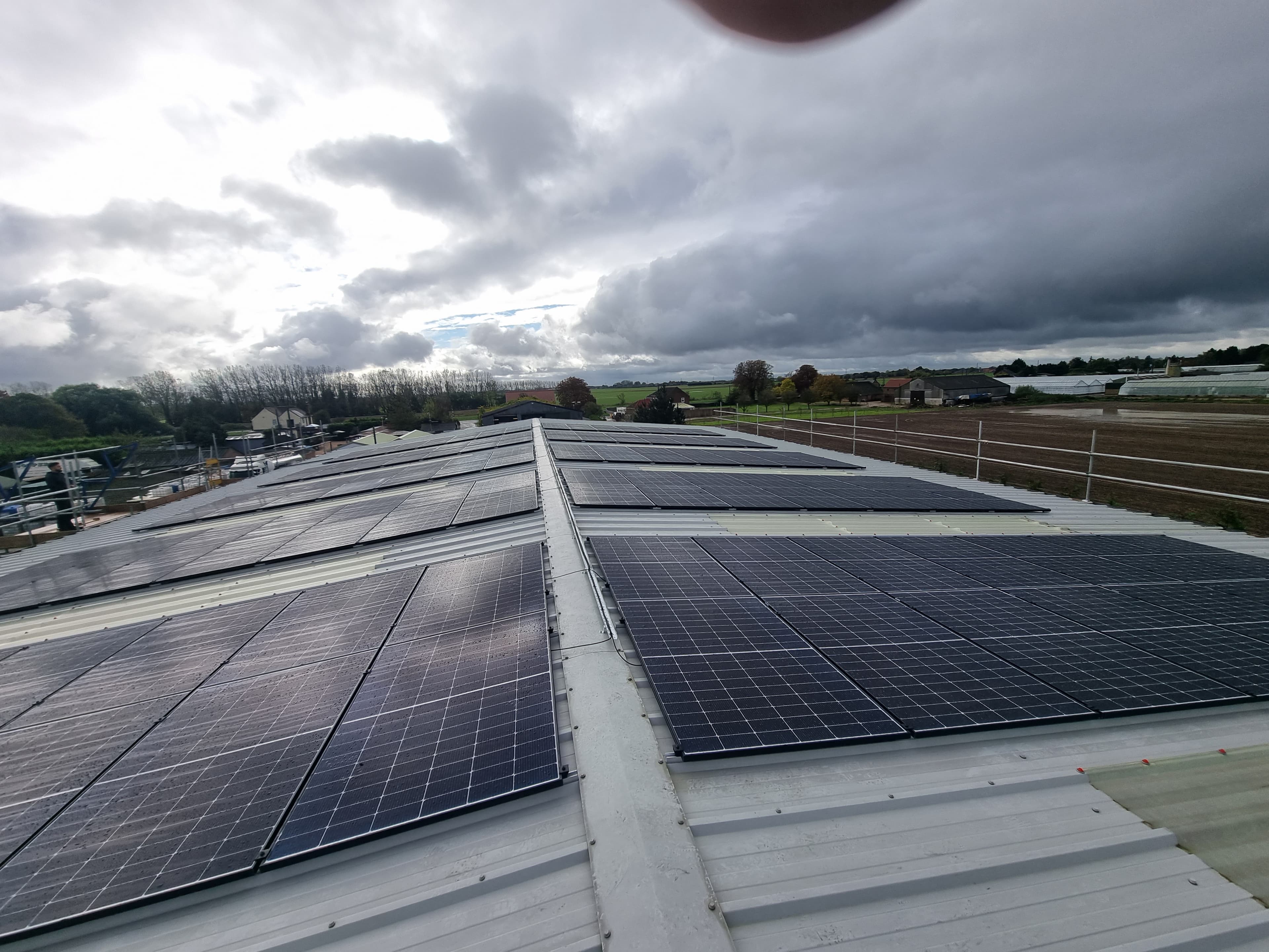 Solar panels installed on a corrugated farm building roof with Lincolnshire countryside beyond