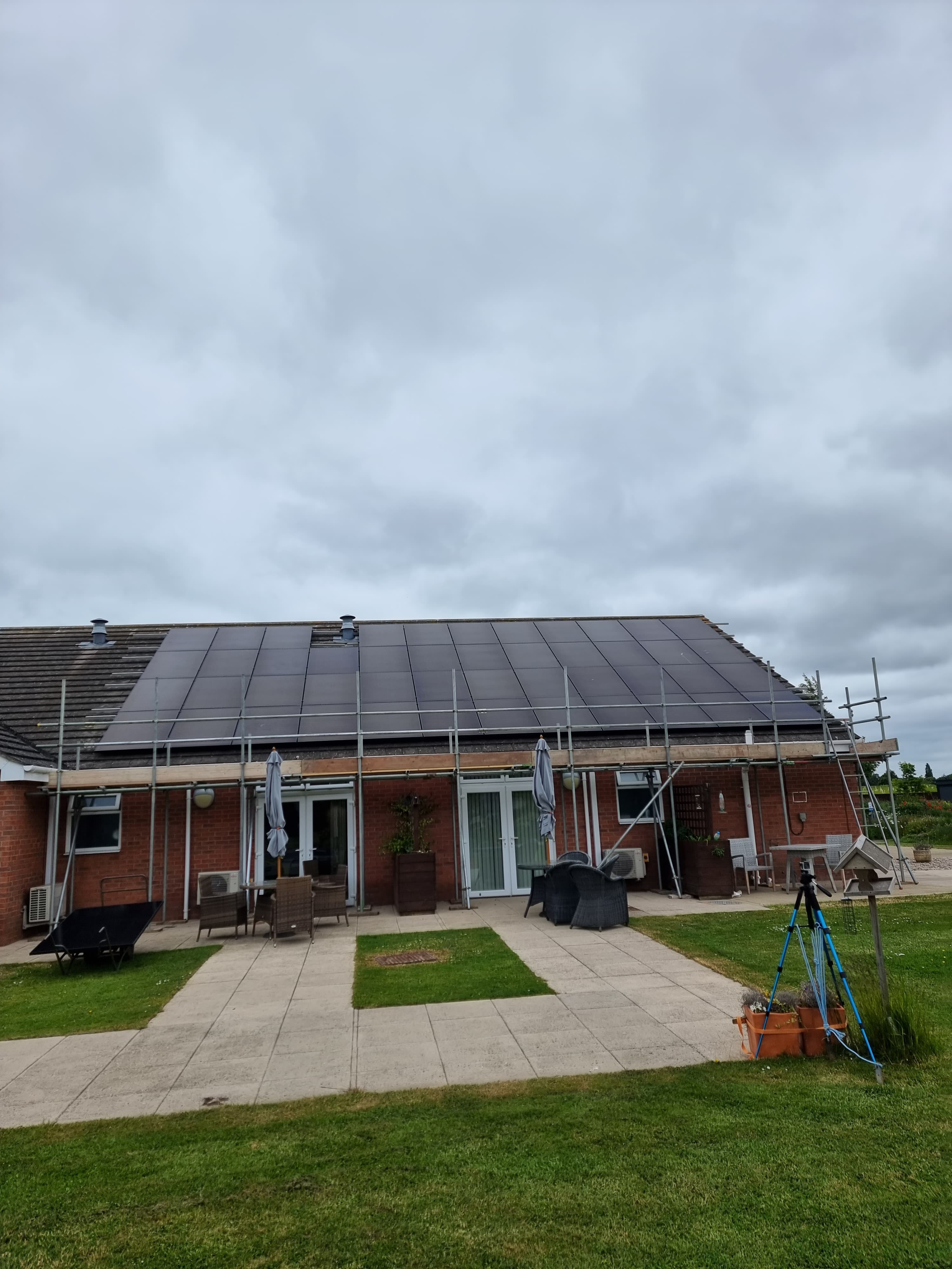 Large solar panel array on a red brick house with patio and garden